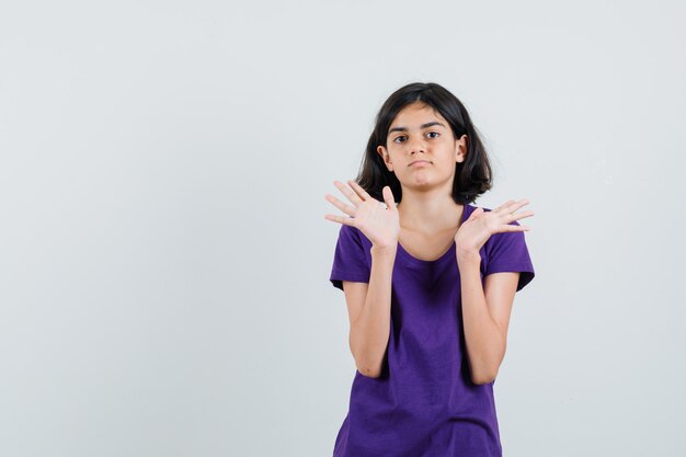 Little girl in t-shirt raising open palms and looking confident ,