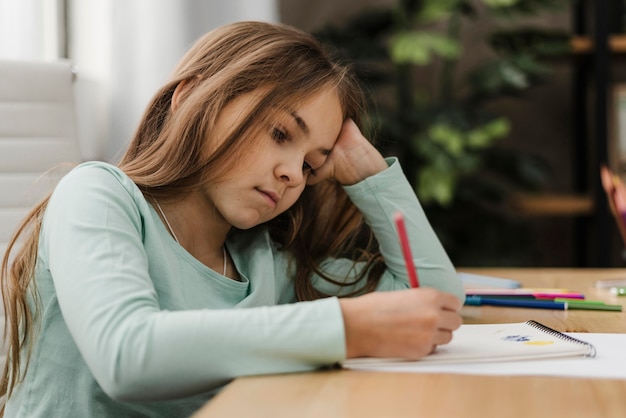 Little girl taking notes while being bored at home