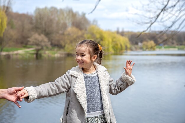 A little girl on a walk in the park in early spring holds her dad's hand.