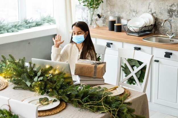 Little girl wearing protective mask on Christmas tree background. Sad child face with surgical mask. Christmas festive and social distancing during covid-19 pandemic concept.