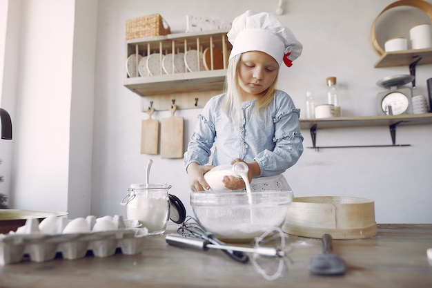 Little girl in a white shef hat cook the dough for cookies