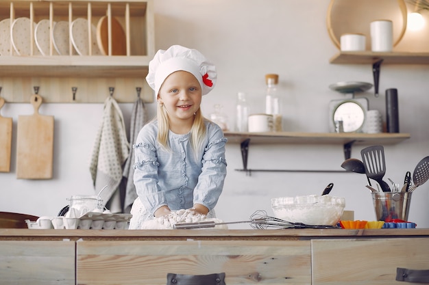 Little girl in a white shef hat cook the dough for cookies