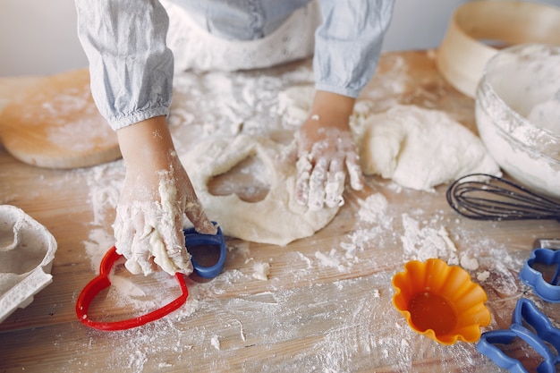 Little girl in a white shef hat cook the dough for cookies