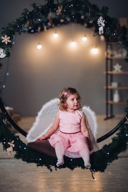 Free Photo little girl with angel wings sitting on fir wreath.