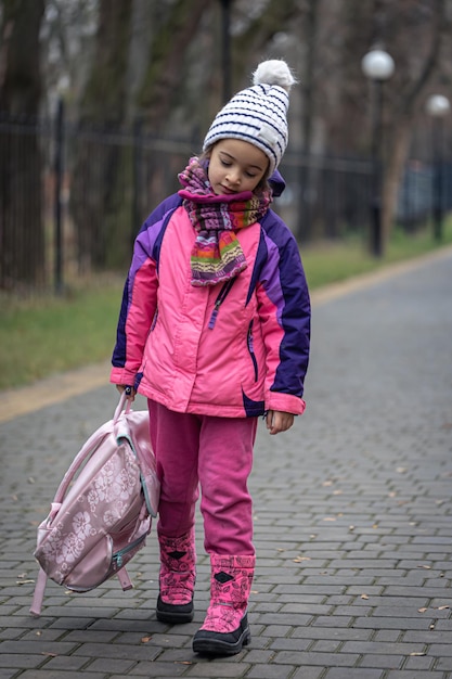 Free Photo little girl with a backpack in a jacket and a hat near the school