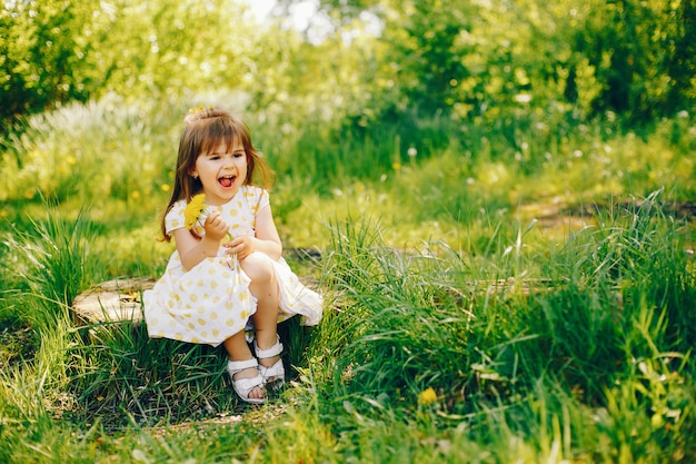 a little girl with beautiful long hair and in a yellow dress is playing in the summer park 