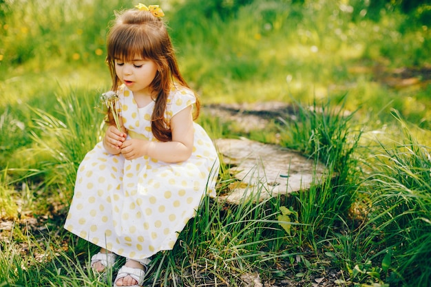 a little girl with beautiful long hair and in a yellow dress is playing in the summer 