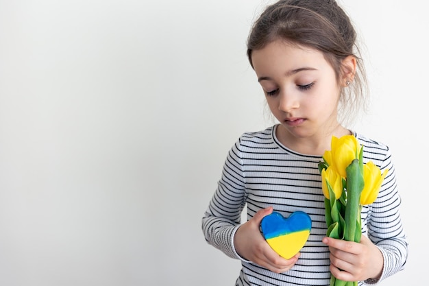 Free photo little girl with a bouquet of tulips and a heart with the flag of ukraine