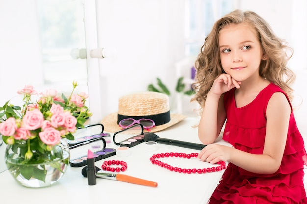 Free Photo a little girl with cosmetics. she is in mother's bedroom, sitting near the mirror.