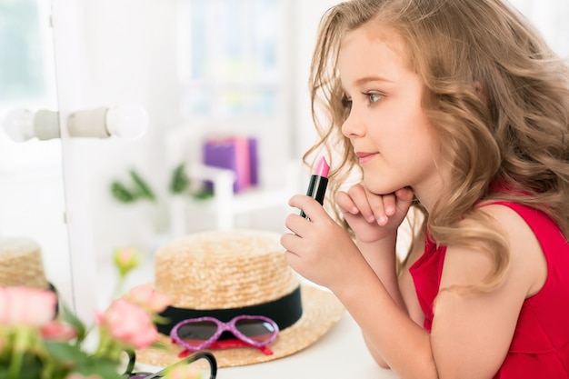 Free photo a little girl with cosmetics sitting near the mirror.