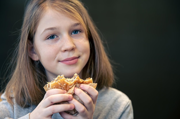 A little girl with freckles eats a burger