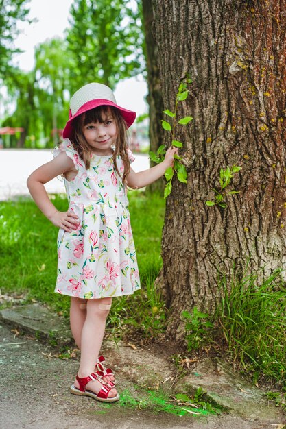 Little girl with one hand leaning on a tree