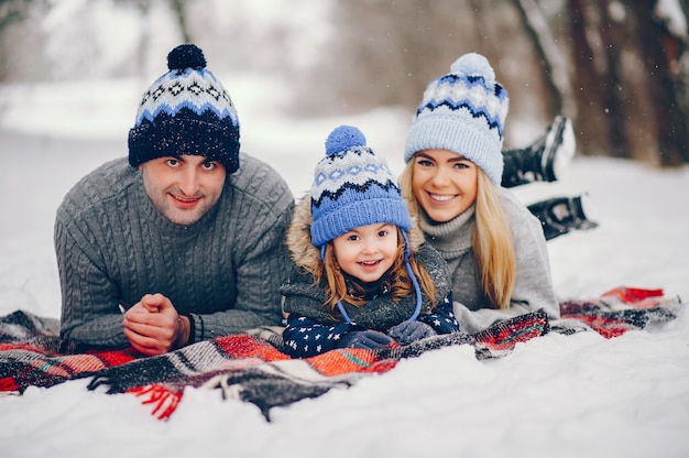 Little girl with parents sitting on a blanket in a winter park