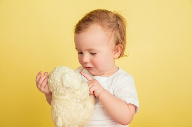 Little girl with plushie isolated on yellow studio wall