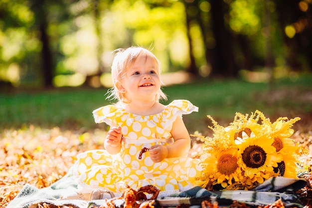 Free Photo little girl in yellow spotted dress sits on the blanket in the park 