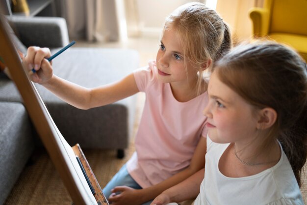 Little girls drawing together at home on easel