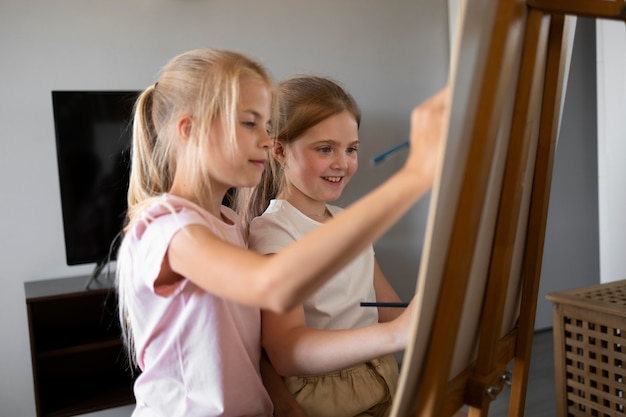 Free photo little girls drawing using easel at home together