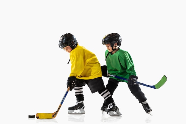 Little hockey players with the sticks on ice court and white  wall. Sportsboys wearing equipment and helmet practicing. Concept of sport, healthy lifestyle, motion, movement, action.