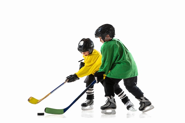 Little hockey players with the sticks on ice court and white  wall. Sportsboys wearing equipment and helmet practicing. Concept of sport, healthy lifestyle, motion, movement, action.