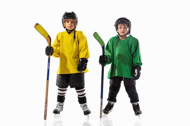 Little hockey players with the sticks on ice court and white  wall. Sportsboys wearing equipment and helmet practicing. Concept of sport, healthy lifestyle, motion, movement, action.