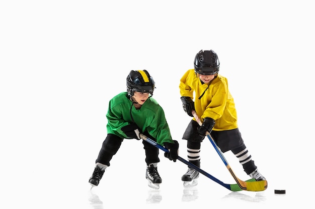 Little hockey players with the sticks on ice court and white  wall. Sportsboys wearing equipment and helmet practicing. Concept of sport, healthy lifestyle, motion, movement, action.