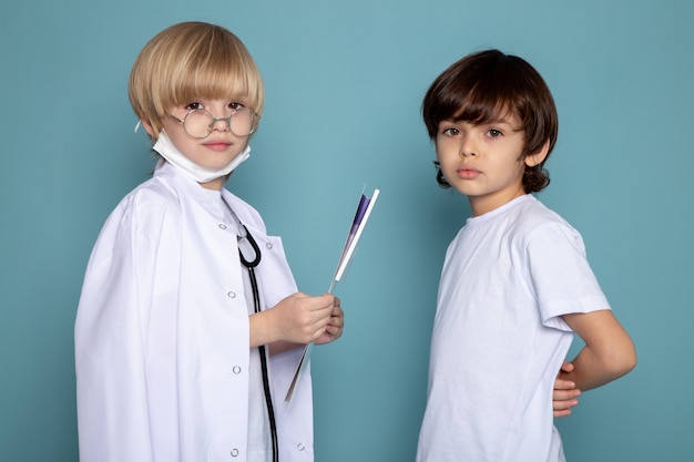 Free photo little kids cute adorable looking at at the camera one in white doctor suit and other in white t-shirt on blue wall