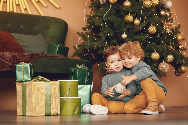 Little kids near christmas tree in a gray sweater