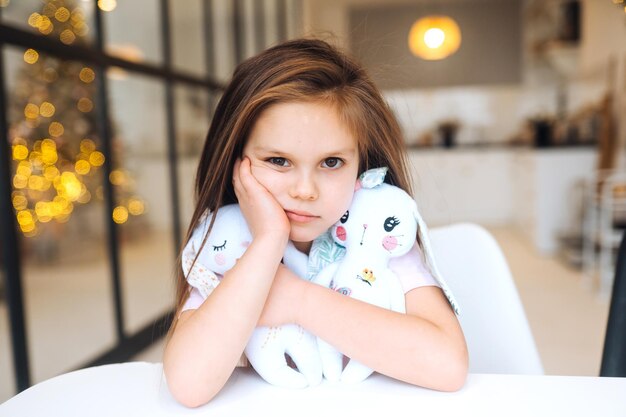 Little sad girl hugging favorite toy while sitting at table happy childhood