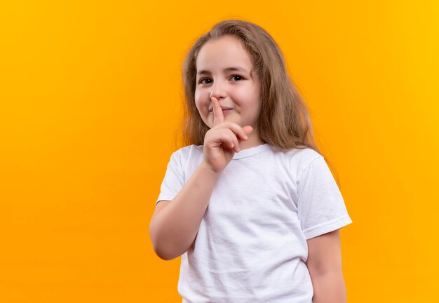 little school girl wearing white t-shirt showing silence gesture on isolated orange wall