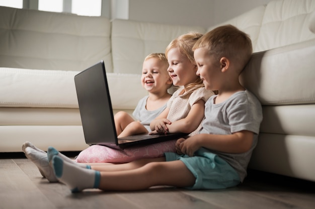 Little sibbling sitting on floor and looking at laptop