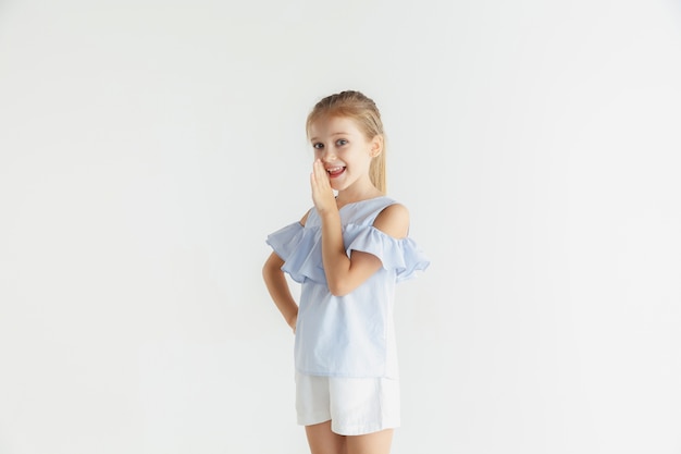 Little smiling girl posing in casual clothes on white wall