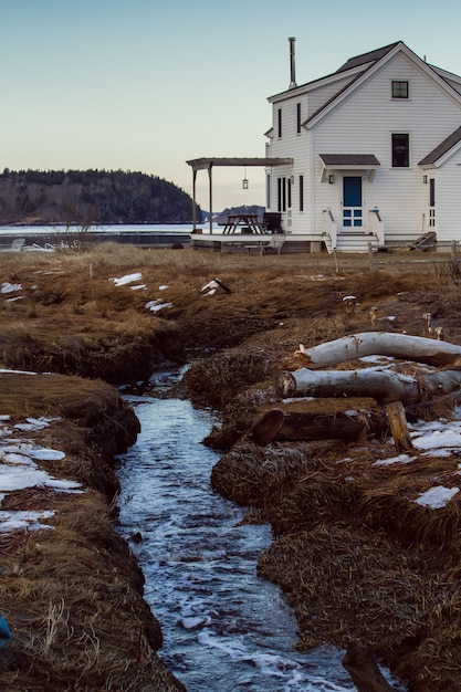 Little stream flowing through the land by a big white house with forest in the background