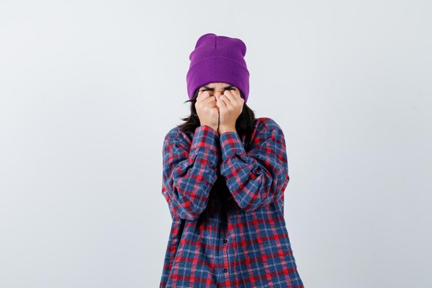 Little woman in checkered shirt and beanie standing in scared pose and looking frightened