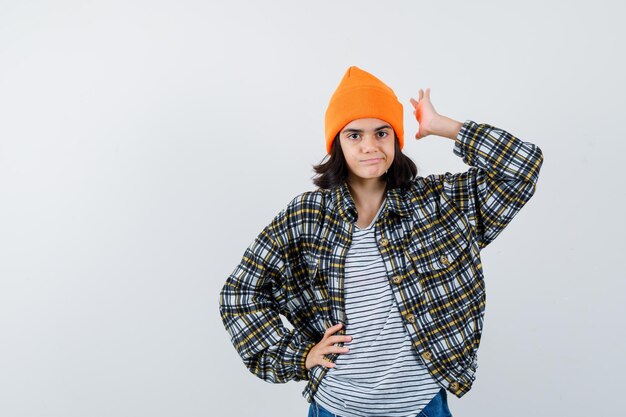 Little woman in t-shirt jacket beanie keeping hand on hip while raising