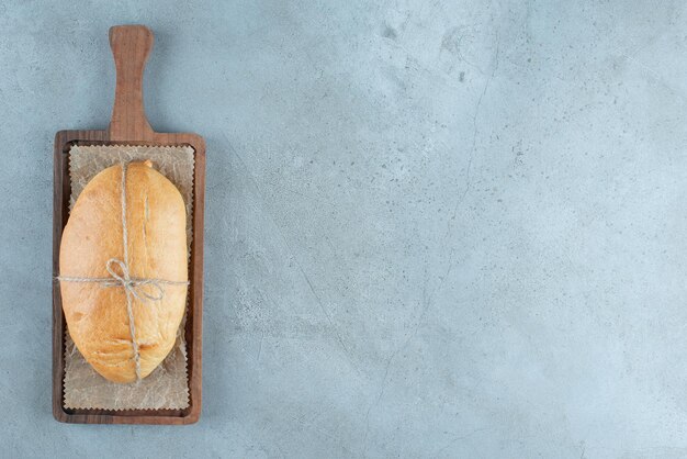 Loaf of bread tied with rope on wooden board.