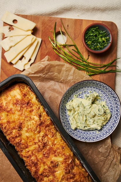 Free photo loaf of cheese bread with herbal butter on a wooden plate with herbs