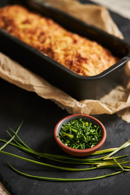 Loaf of cheese bread with herbal butter on a wooden plate with herbs