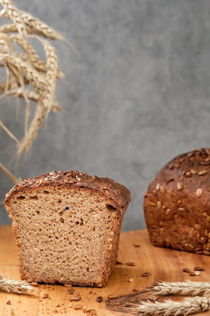 Loaf of wheat-rye sourdough bread with sunflower seeds on a cutting board. Freshly baked dark bread halves, close-up selective focus. Wheat ears on the table