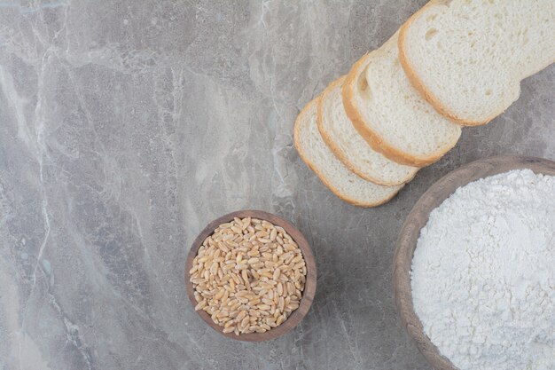 A loaf of white bread with oat grains and flour on marble background.