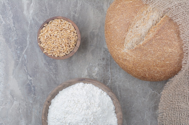 A loaf of white bread with oat grains and flour on marble surface