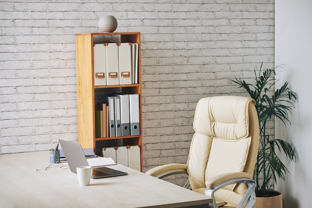 Loft-style office with laptop sitting on desk, executive chair and document folders on shelves