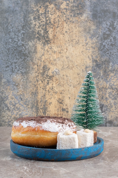 Lokums, donut and a tree figurine on a blue platter on marble.