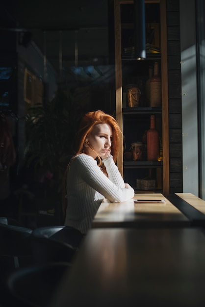 A lone young woman sitting near the window with mobile phone on table