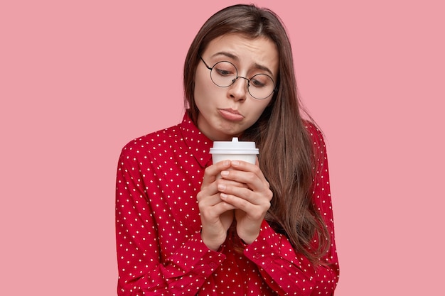 Free Photo lonely dejected woman purses lower lip, holds disposable cup of hot drink, feels sad, being in low spirit