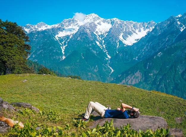 Free Photo lonely male lying down and sunbathing on a meadow with mountains