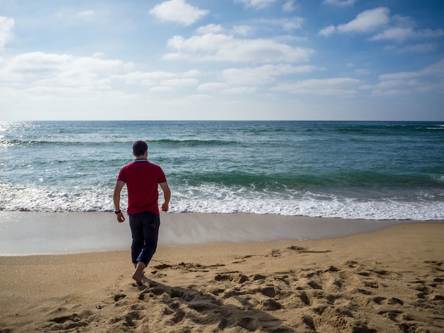 Lonely male walking on the beach under the beautiful cloudy sky