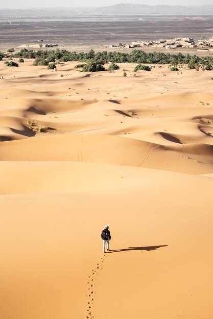 Lonely person walking in a desert near sand dunes on a sunny day