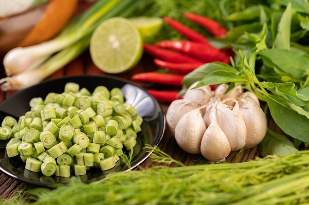 Long beans, garlic, chili, lime, scallion and cha-om are placed on a wooden table