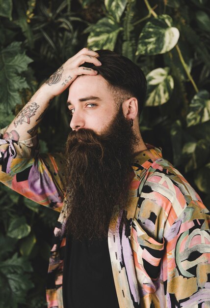 Long bearded young man with hands on head looking at camera