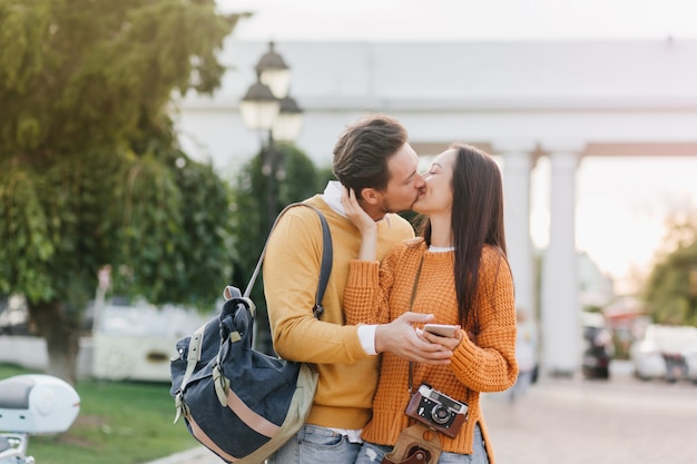 Long-haired brunette woman with camera kissing her boyfriend on blur city